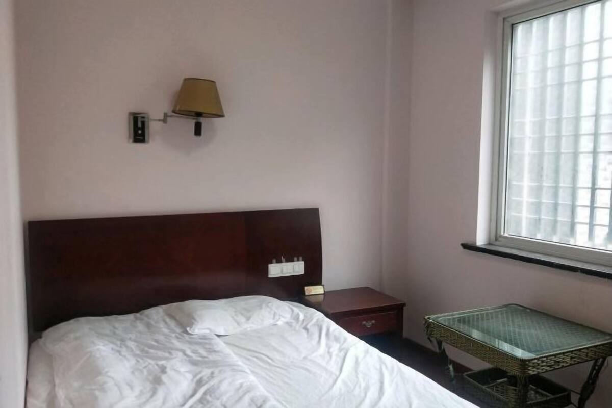 A hotel room with a bed, a nightstand, a lamp, a small table, and a window.