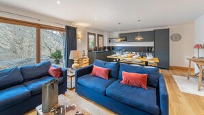 Un soggiorno moderno con un ampio divano blu, un'area pranzo con tavolo in legno e una cucina sullo sfondo.