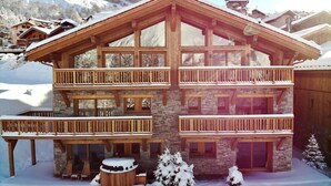Un chalet in legno a più piani con balconi, pareti in pietra e un paesaggio innevato.