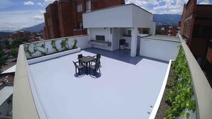 Terraza en la azotea con mesa y sillas, rodeada por un muro blanco con vegetación.