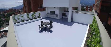 Terraza en la azotea con mesa y sillas, rodeada por un muro blanco con vegetación.