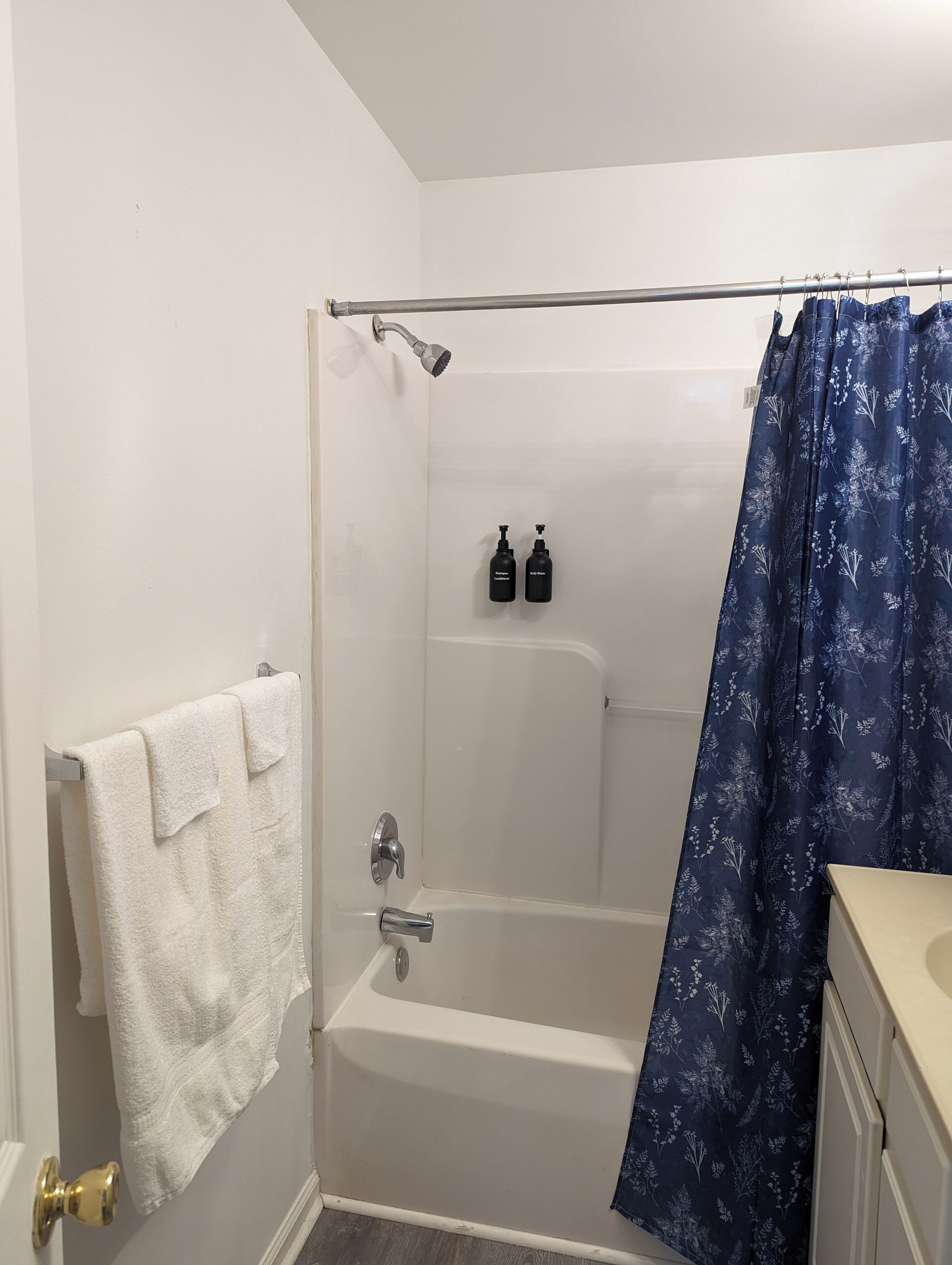 Une salle de bain avec une baignoire, un rideau de douche et deux bouteilles de shampoing et d’après-shampoing.