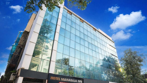 Um hotel moderno com fachada de vidro, área de recepção e uma placa com a inscrição "HOTEL MAHARAJA INN".