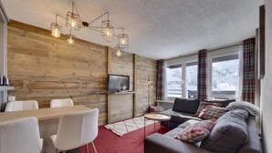 A cozy living room with a wooden wall, a red carpet, a grey sofa, and a TV on a wooden shelf. - 2nd floor, balcony, tv, ski locker, 41m², Tignes (Tignes)