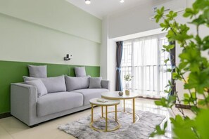 Una sala moderna con un sofá gris, dos mesitas redondas y un ventanal con cortinas.