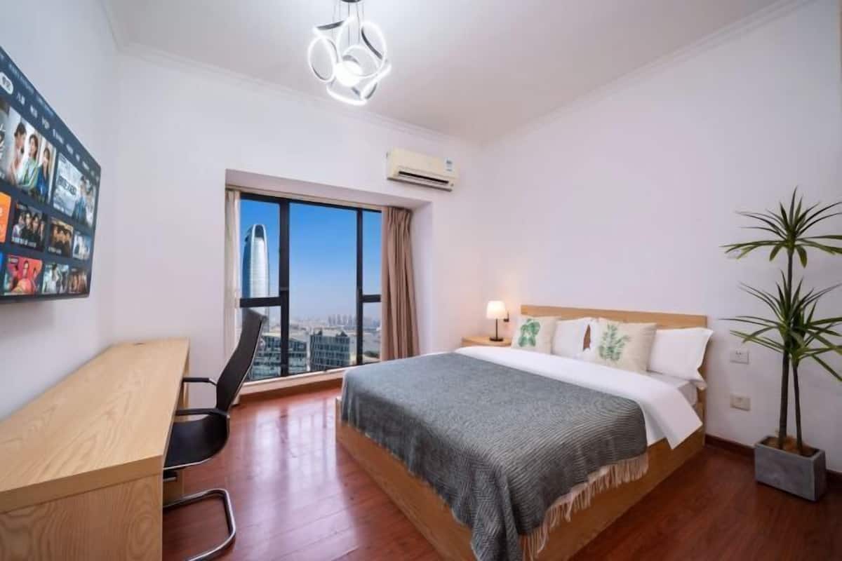 Quarto de hotel com cama, escrivaninha, cadeira e uma grande janela com vista para a cidade.