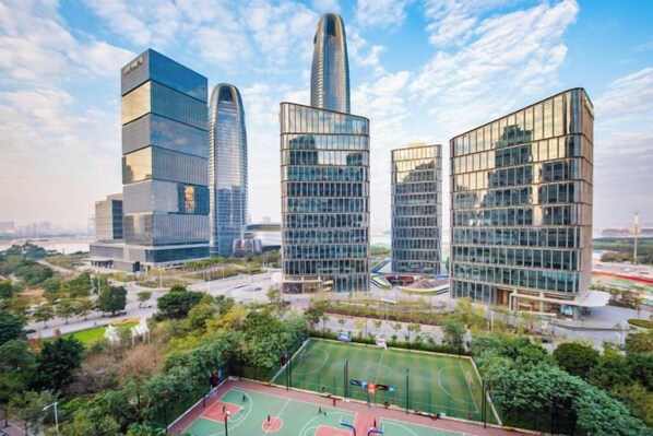 Un moderno complejo de edificios con varias torres altas, rodeado de áreas verdes y una cancha deportiva.