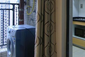 Un espace buanderie comprenant un lave-linge, un étendoir et une fenêtre donnant sur des immeubles.