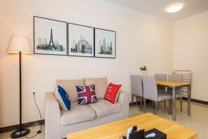 A hotel room with a sofa, a dining table, and a lamp. There are three framed pictures on the wall.