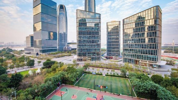 Un quartier urbain moderne, avec de hauts immeubles, un terrain de basketball et de nombreux espaces verts.