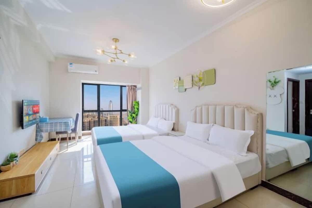 Quarto de hotel com duas camas, uma escrivaninha, uma cadeira, uma televisão e uma janela grande.