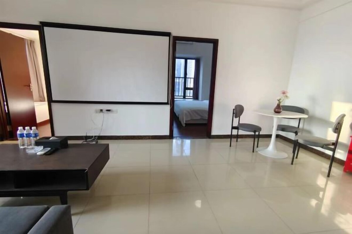 Ein Hotelzimmer mit einem Bett, einem kleinen Tisch mit Stuhl, einer Whiteboard-Tafel und Blick auf ein weiteres Zimmer.