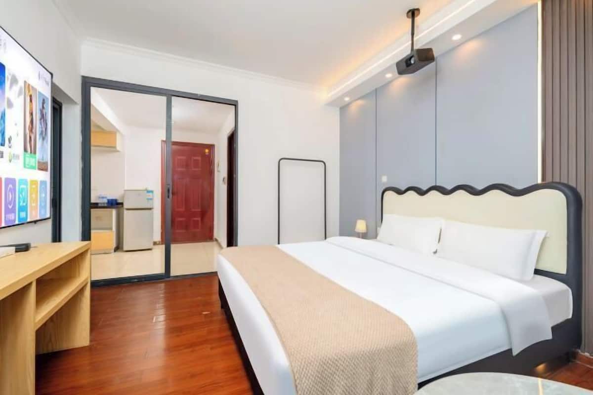 Quarto de hotel com cama, secretária, televisão e porta para um banheiro.