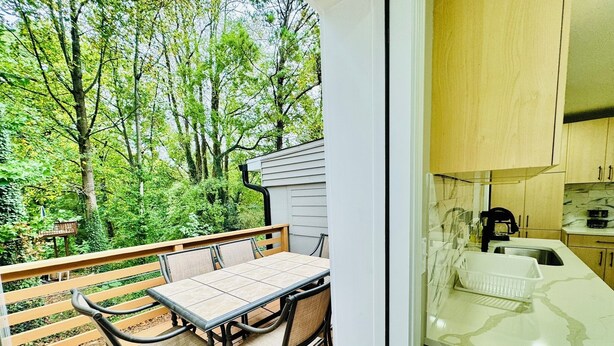 A balcony with a table and chairs, a view of trees, and a kitchen area with cabinets and a countertop. - Modern Brick Ranch Retreat NEW Renovation (Mableton)