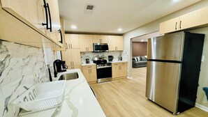 A modern kitchen with light wood cabinets, a stainless steel refrigerator, a microwave, and a sink with a marble countertop. - Modern Brick Ranch Retreat NEW Renovation (Mableton)