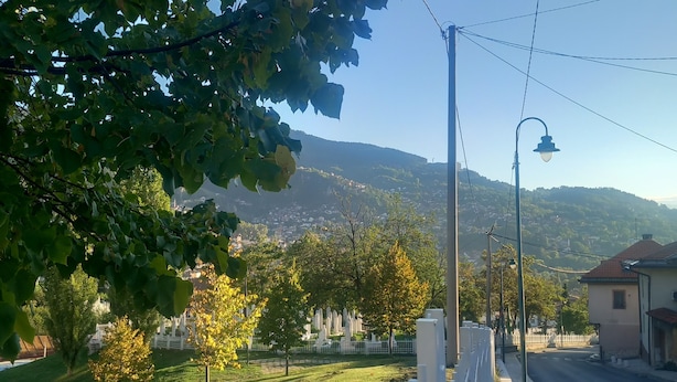 A street with a white fence, a lamppost, and a grassy area with trees. - Budget Rooms (Sarajevo)