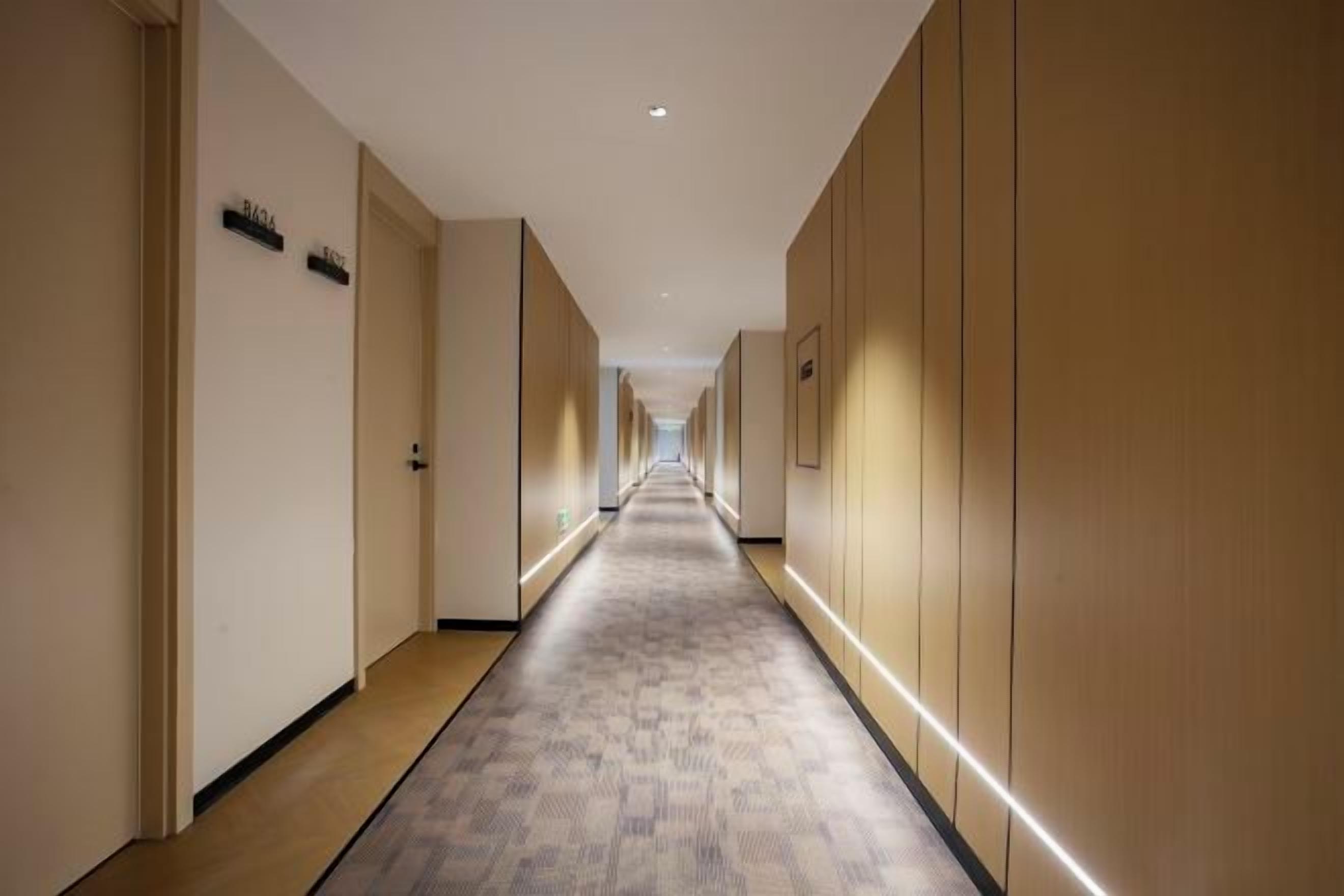 Un pasillo de hotel con puertas a ambos lados, suelo alfombrado y una tira de luces a lo largo del techo.