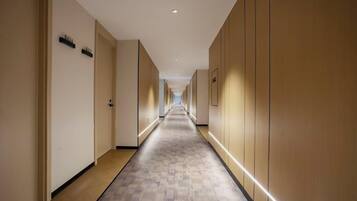 Un pasillo de hotel con puertas a ambos lados, suelo alfombrado y una tira de luces a lo largo del techo.