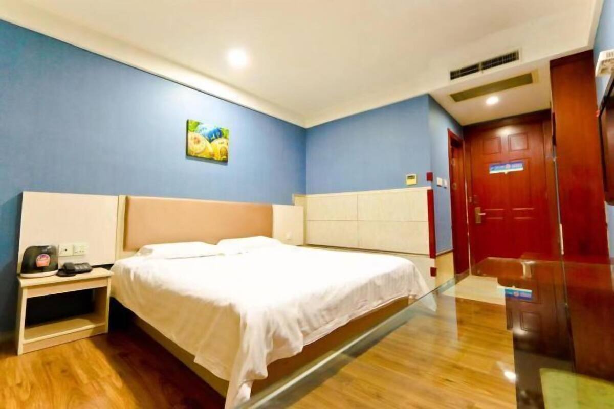 A hotel room with a bed, bedside table, and a red door.