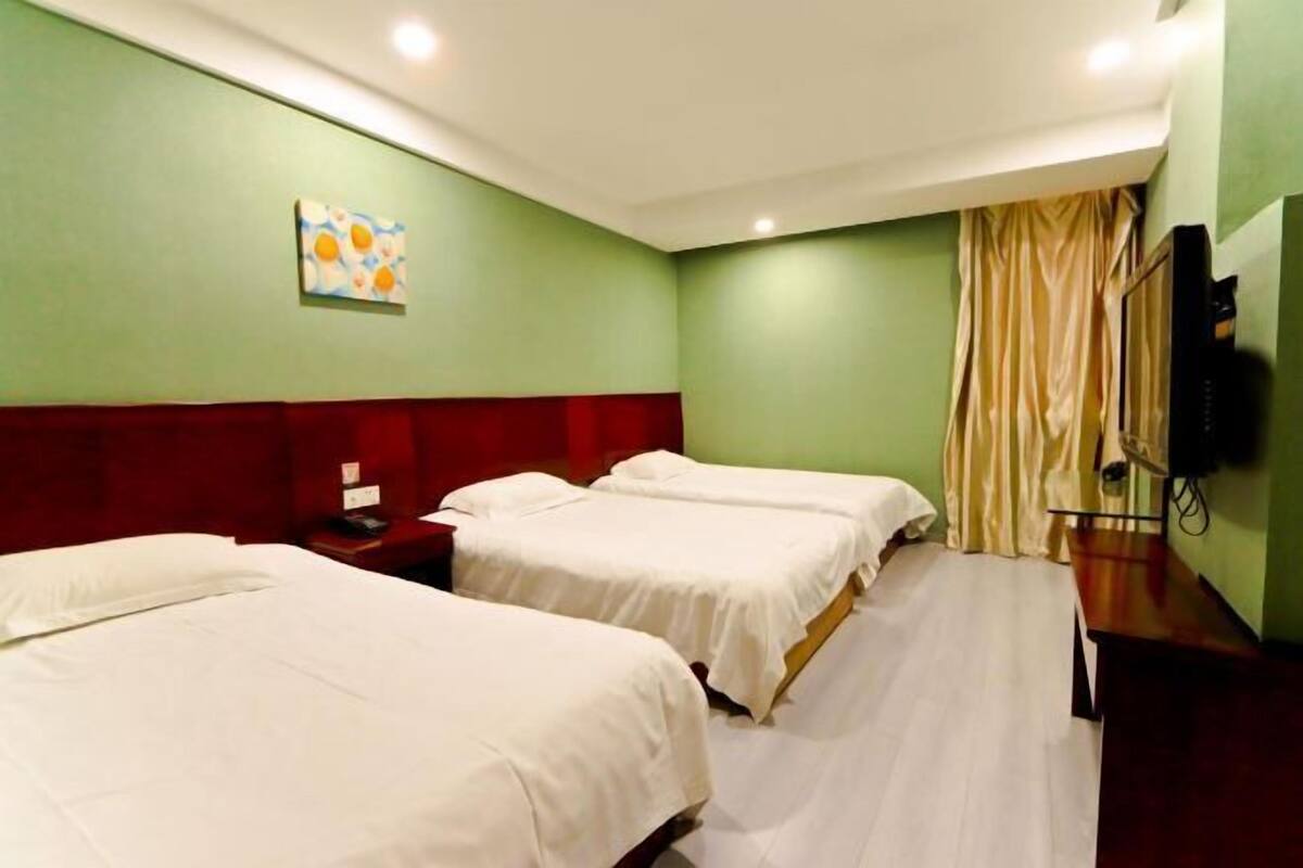 A hotel room with two beds, a red headboard, a television, and a painting on the wall.