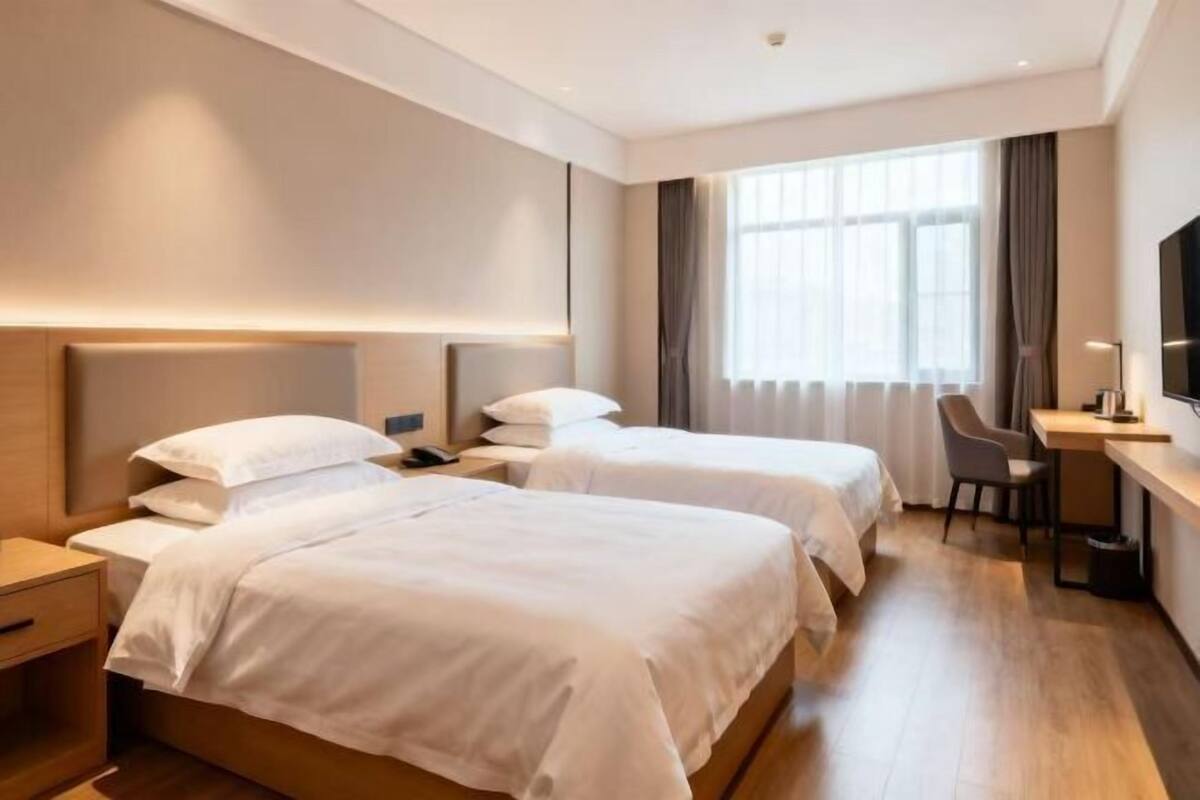 A hotel room with two beds, a desk, a chair, and a TV.