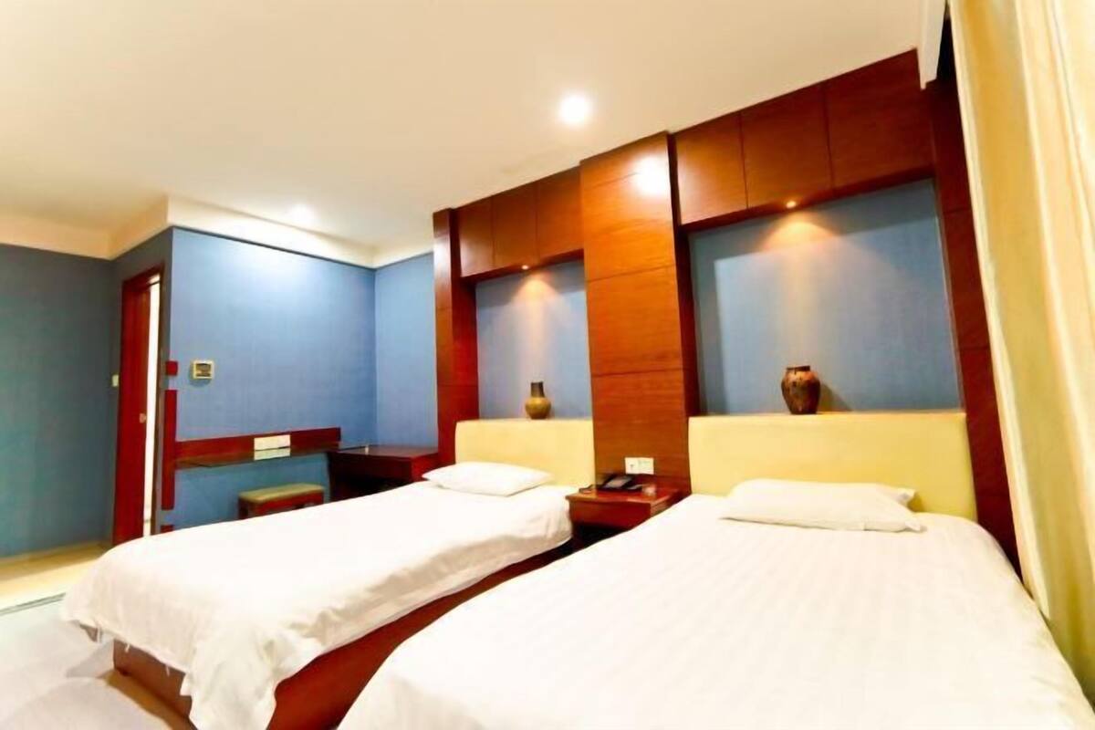 A hotel room with two single beds, wooden headboards, and a small table with a vase.