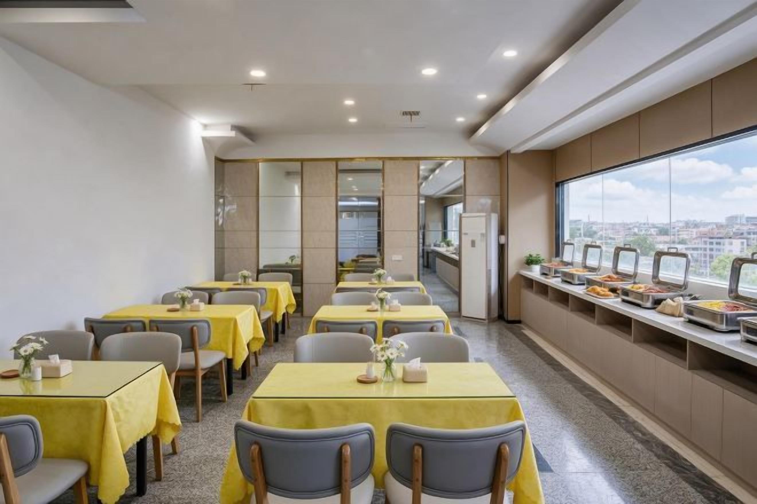 Comedor con mesas, sillas, una barra de buffet y vistas de la ciudad a través de amplias ventanas.