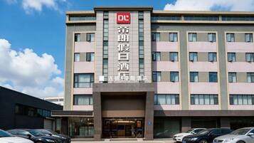 A hotel building with a prominent sign, multiple floors, and a parking lot with several cars.