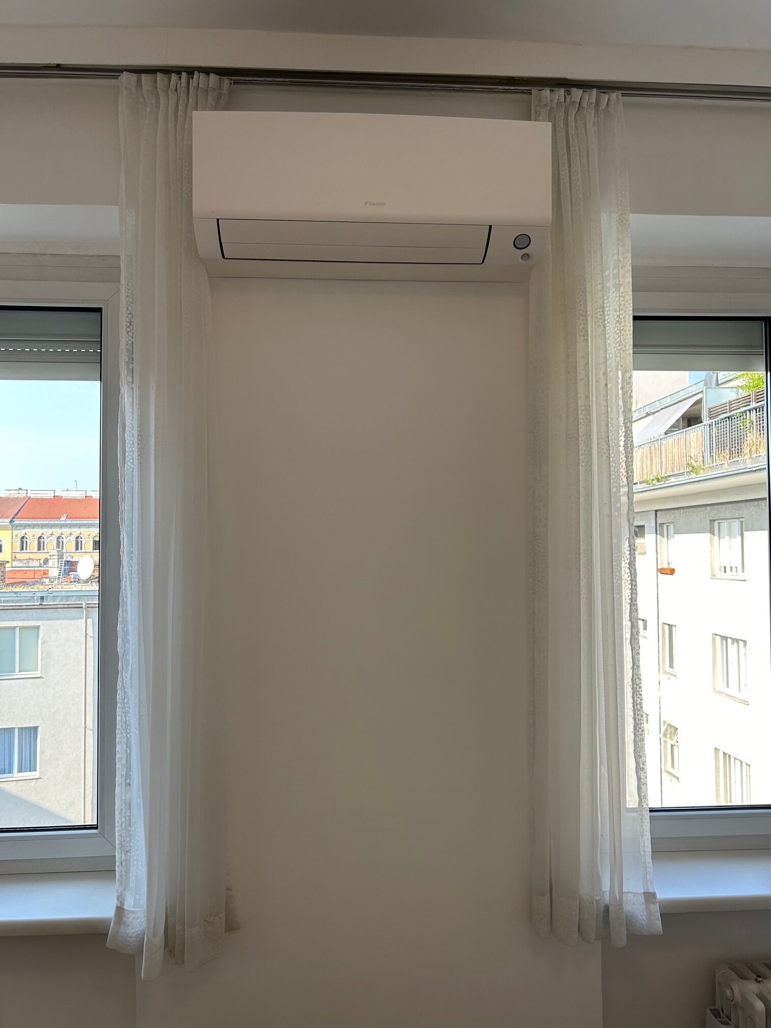 Une pièce dotée d’une grande fenêtre, de rideaux blancs et d’un appareil de climatisation.
