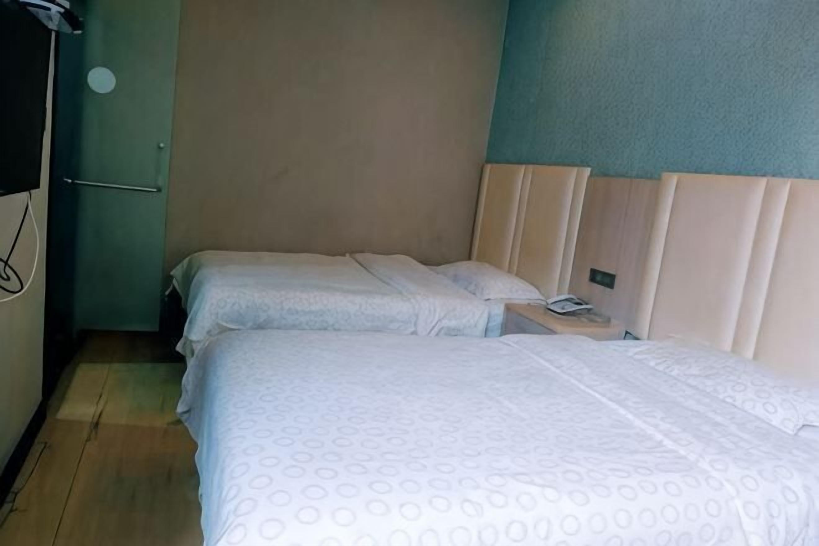 A room with two beds, a wooden floor, a green wall, and a door.