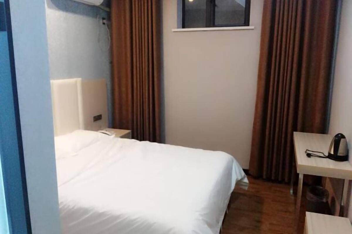 Ein Hotelzimmer mit Bett, Nachttisch, Tisch mit Wasserkocher und Fenster mit Vorhängen.