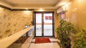 A hotel lobby with marble walls, a reception desk, a red carpet, and a potted plant. - Nanyang Yuyu Inn (Nanyang)