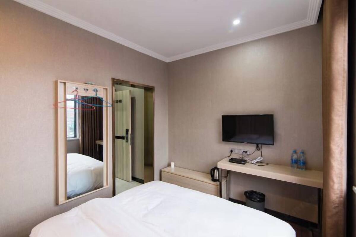 Ein Hotelzimmer mit einem Bett, einem Fernseher, einem Schreibtisch mit Wasserkocher und einem Spiegel.
