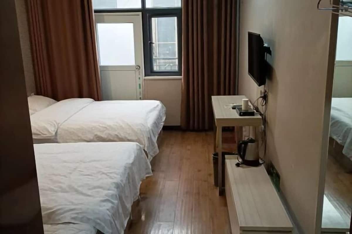 Ein Hotelzimmer mit zwei Betten, einem Schreibtisch mit Fernseher und einem Fenster mit Vorhängen.