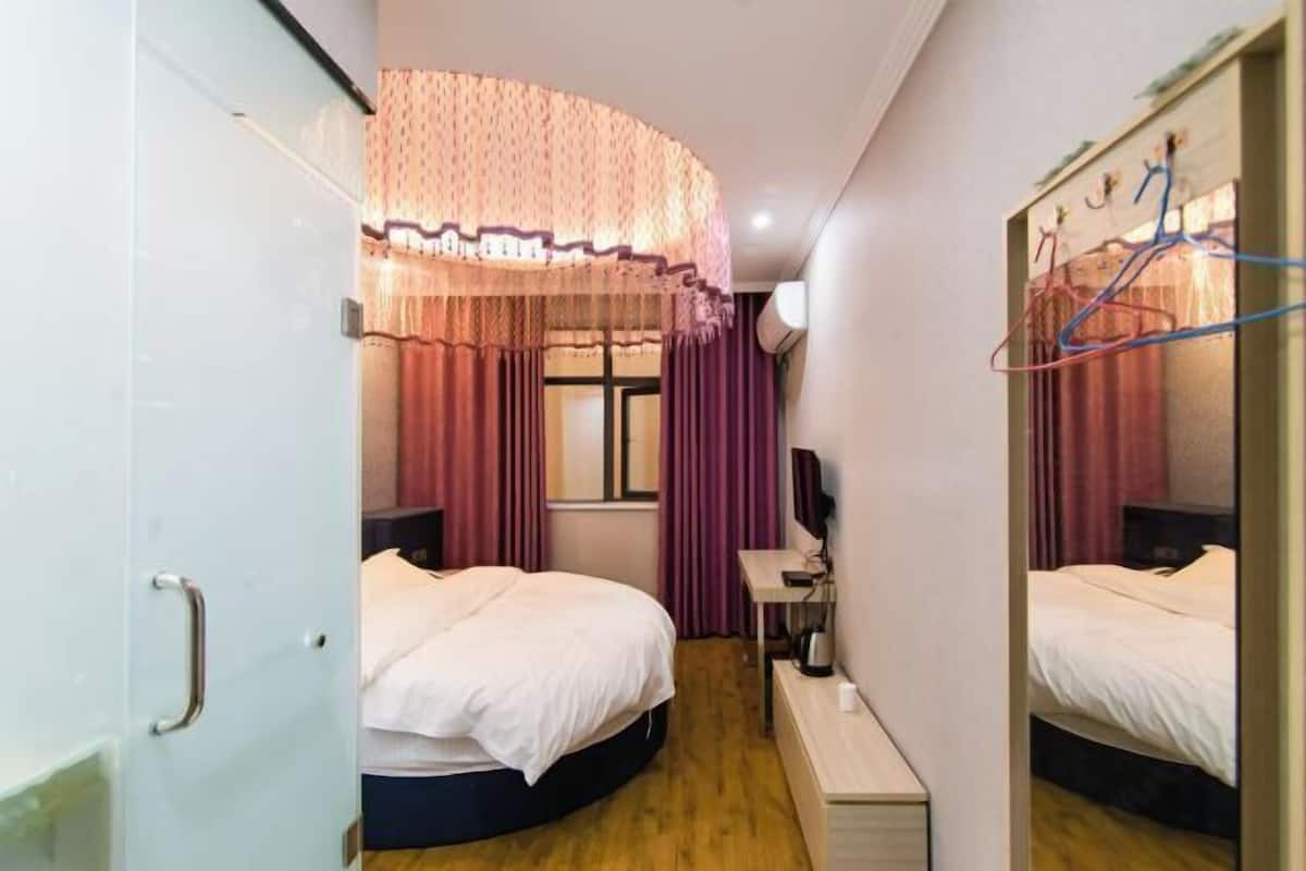 Ein Hotelzimmer mit zwei Betten, einem Schreibtisch, einem Sessel, einem Spiegel und einem Fenster mit Vorhängen.