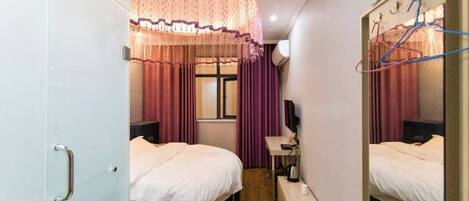 Une chambre d’hôtel avec deux lits, un bureau, une chaise, un miroir et une fenêtre avec des rideaux.