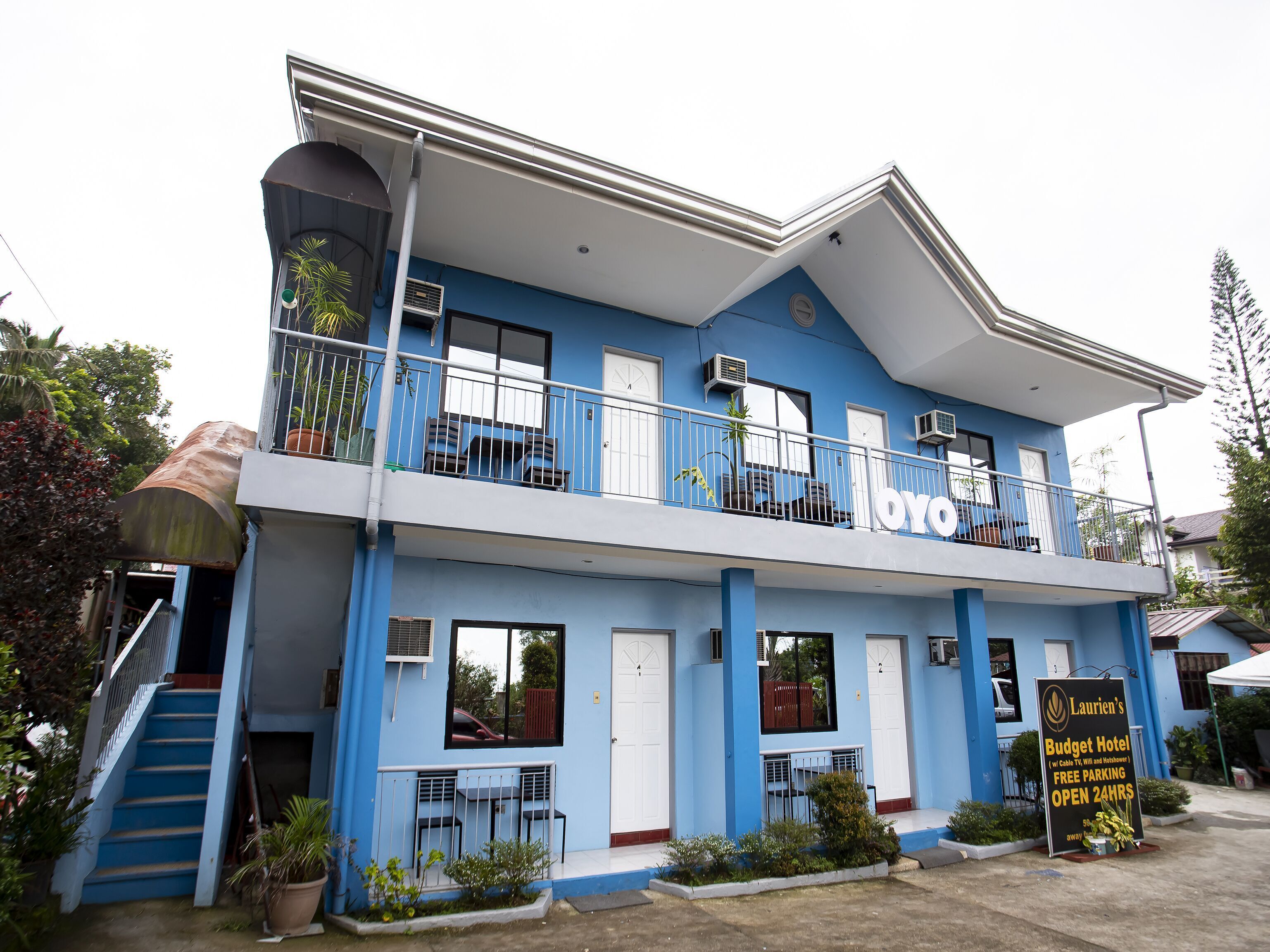 A two-story building with balconies, a sign for Laurien's Budget Hotel, and a staircase leading to the entrance.