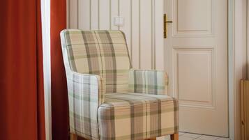 A plaid-patterned armchair in a room with wooden flooring, a white door, and a red curtain.