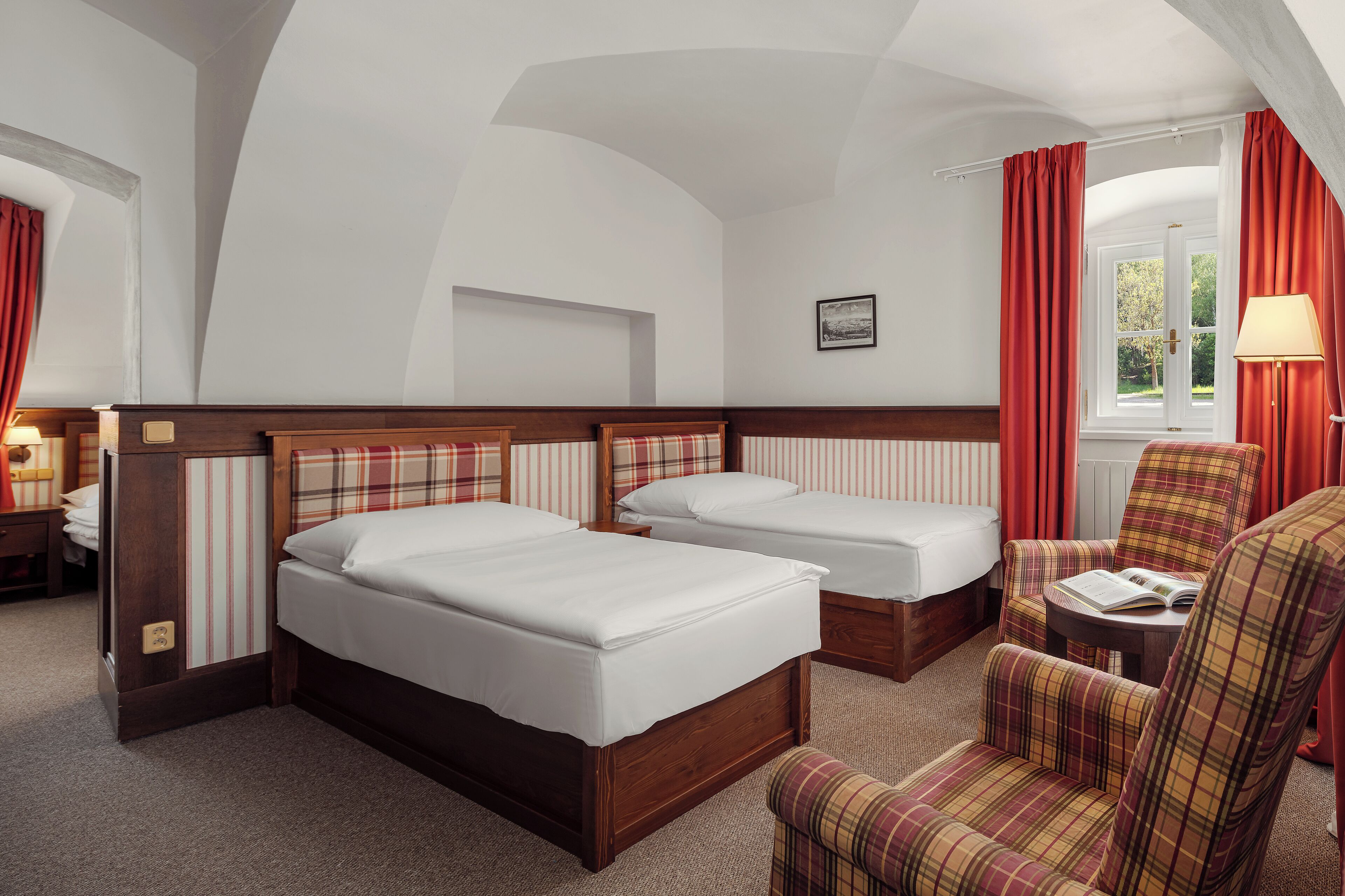 A hotel room with two beds, a chair, a table, and a window with curtains.