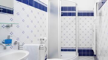 A bathroom with a white sink, a toilet, a glass shower enclosure, and blue and white patterned tiles.