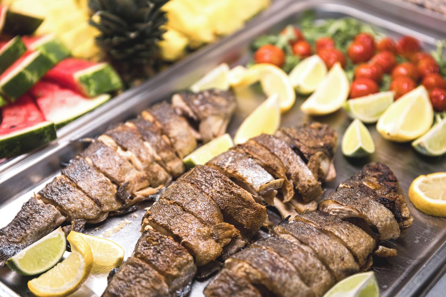Grillattua kalaa, tarjoiltuna limelohkojen ja monenlaisten hedelmien ja vihannesten kanssa yhdellä vadilla.