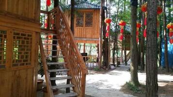 Una estructura de madera con una escalera que lleva a un espacio cubierto, rodeada de árboles y faroles rojos.