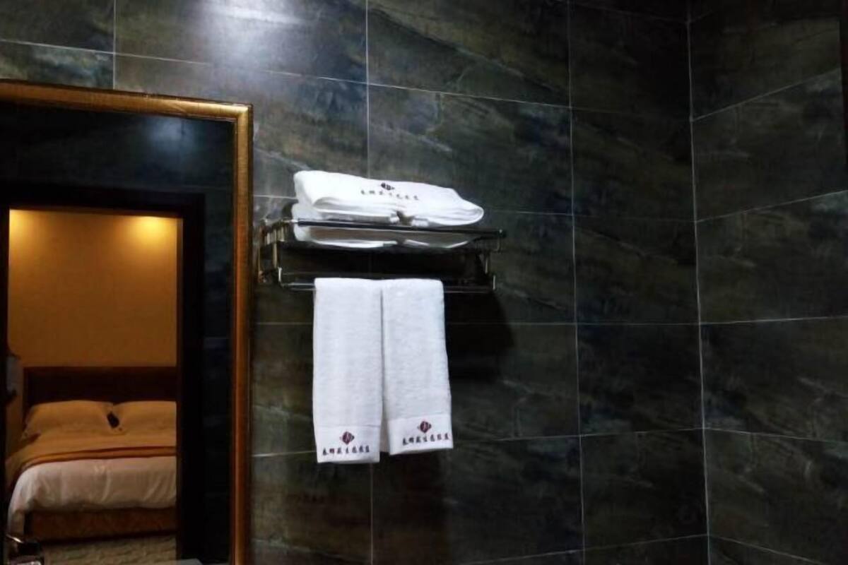 Un baño con paredes de baldosas oscuras, un espejo con marco de madera y un toallero con toallas dobladas y un paño blanco.