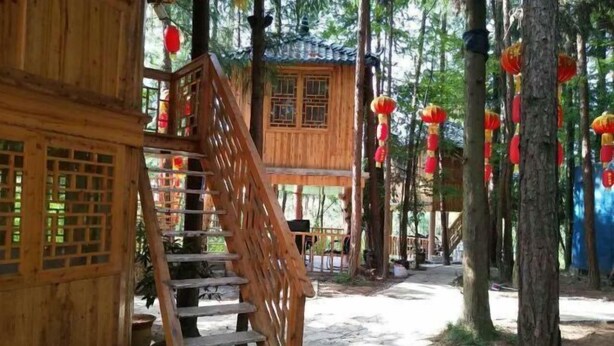 A wooden structure with a staircase leading to a covered area, surrounded by trees and red lanterns. - Lichuan Chunhuiyuan Homestay (Lichuan)