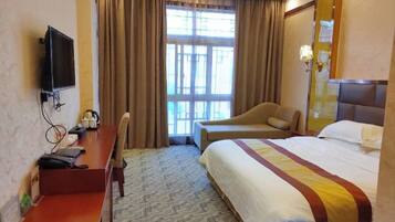 A hotel room with a bed, a desk with a chair, a television, and a window with curtains.