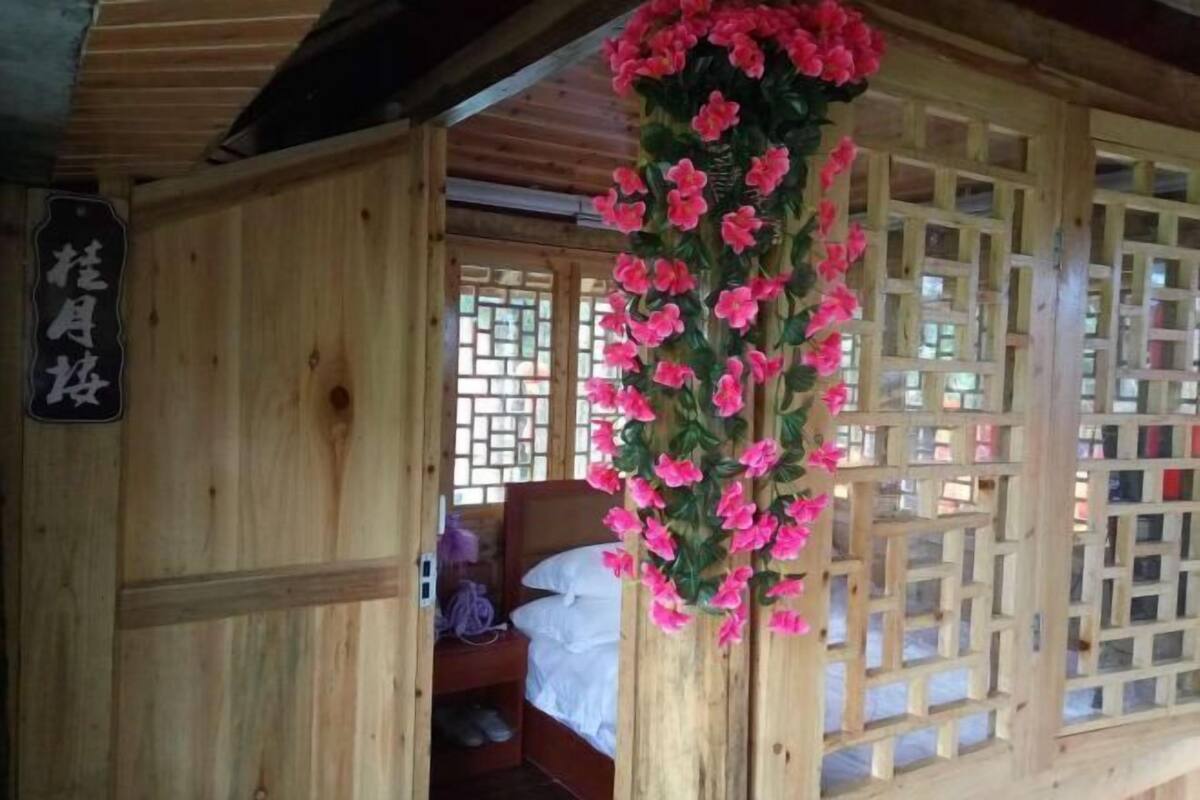 Una habitación de madera con una cama, un adorno floral colgante y una ventana con celosía.
