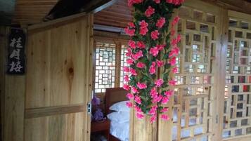 Una habitación de madera con una cama, un adorno floral colgante y una ventana con celosía.