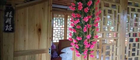 A wooden room with a bed, a hanging floral decoration, and a lattice window.