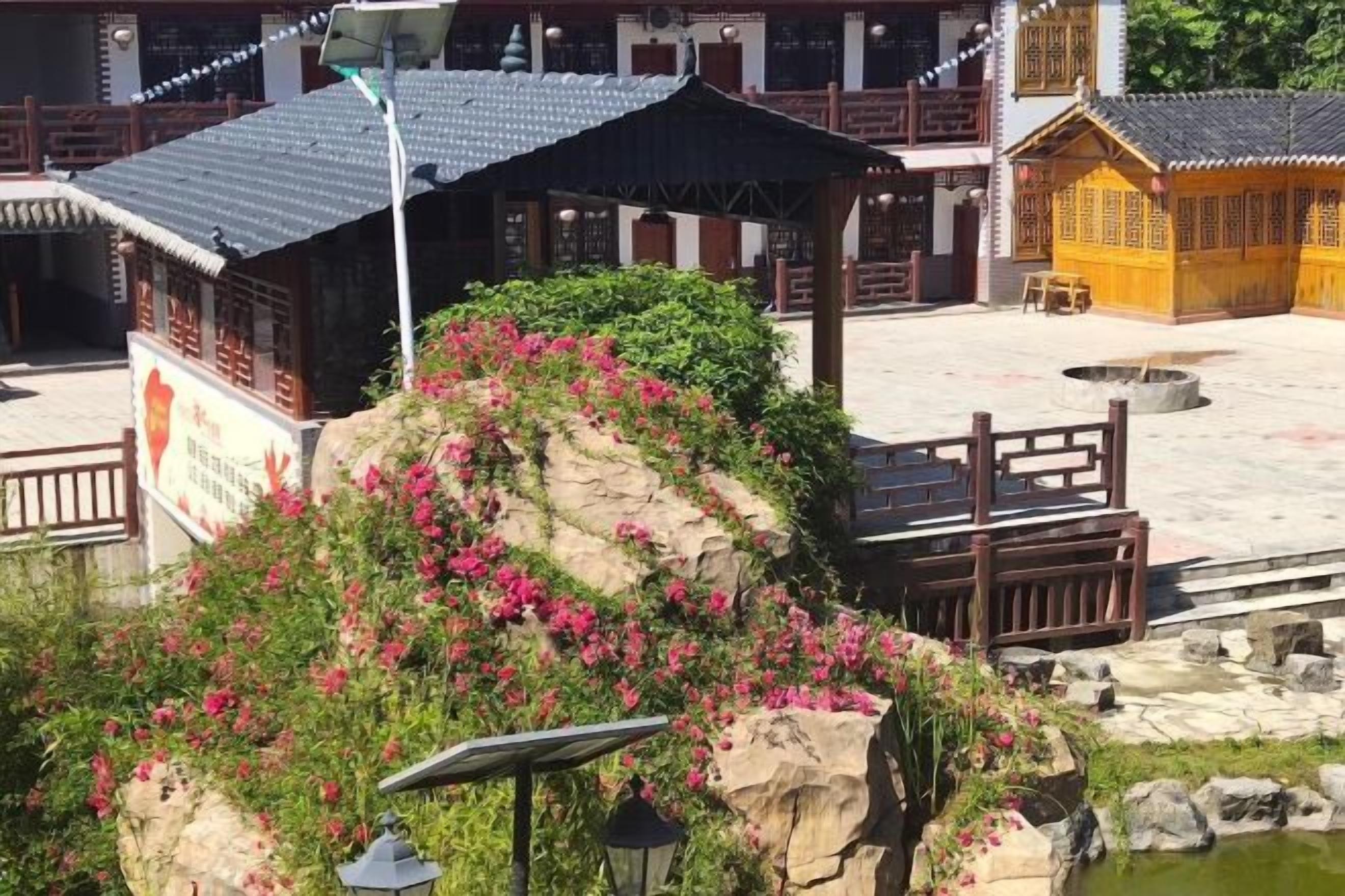 A traditional building with a tiled roof, a wooden fence, and a rock with pink flowers.