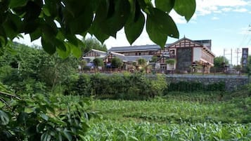 Un bâtiment traditionnel à la façade en bois, entouré de verdure et bordé d’un mur de pierre.